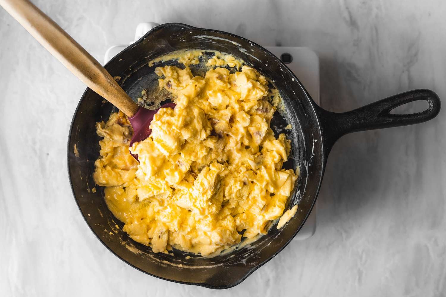 Scrambled eggs gently turned and stirred in a cast iron pan with a rubber spatula
