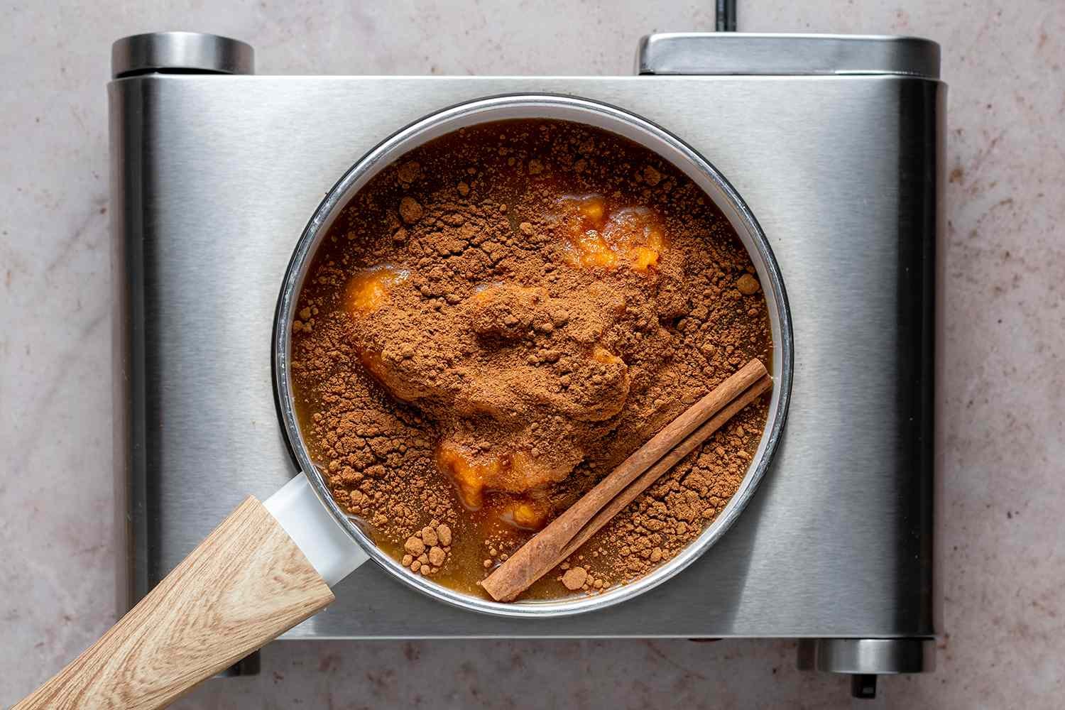 Pumpkin, apple cider, maple syrup, pumpkin pie spice, salt, and cinnamon stick in a pan on a burner