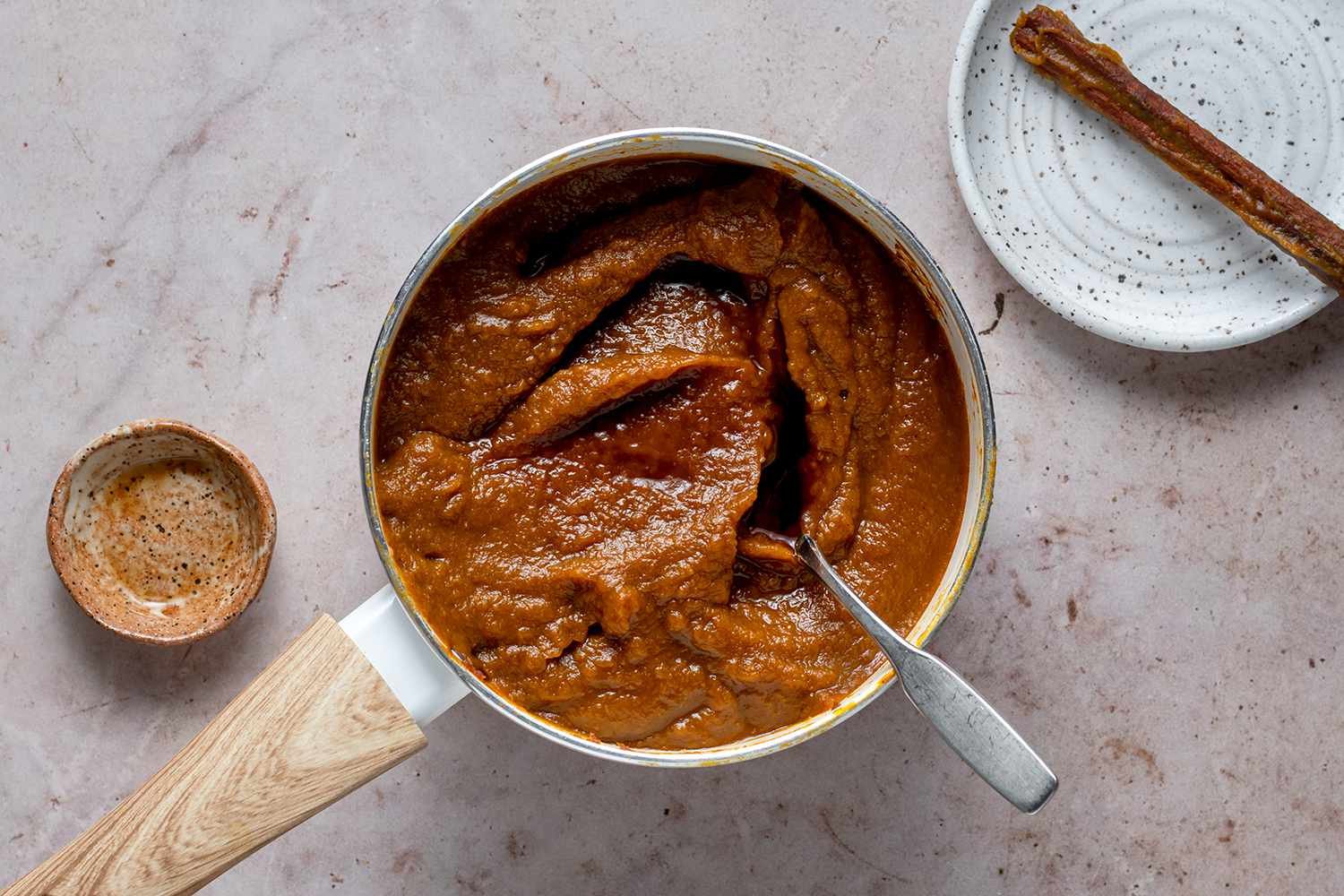 Pumpkin Butter in a pan with vanilla, and a cinnamon stick on a plate