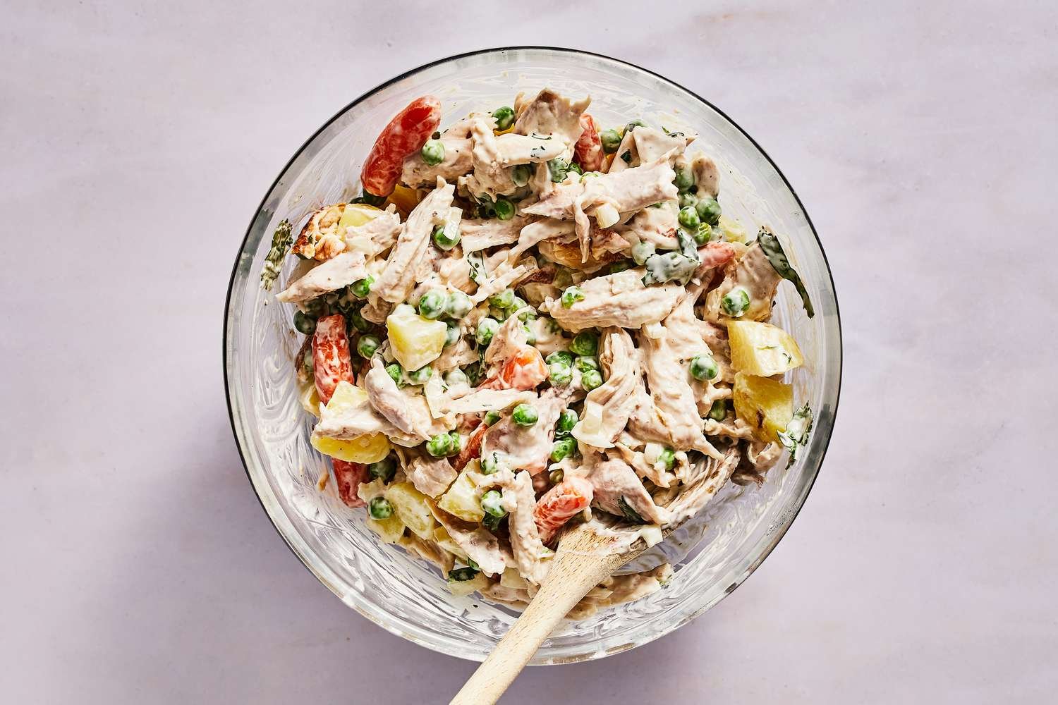 A bowl of Mexican chicken salad, with cooked potatoes being folded in with a wooden spoon