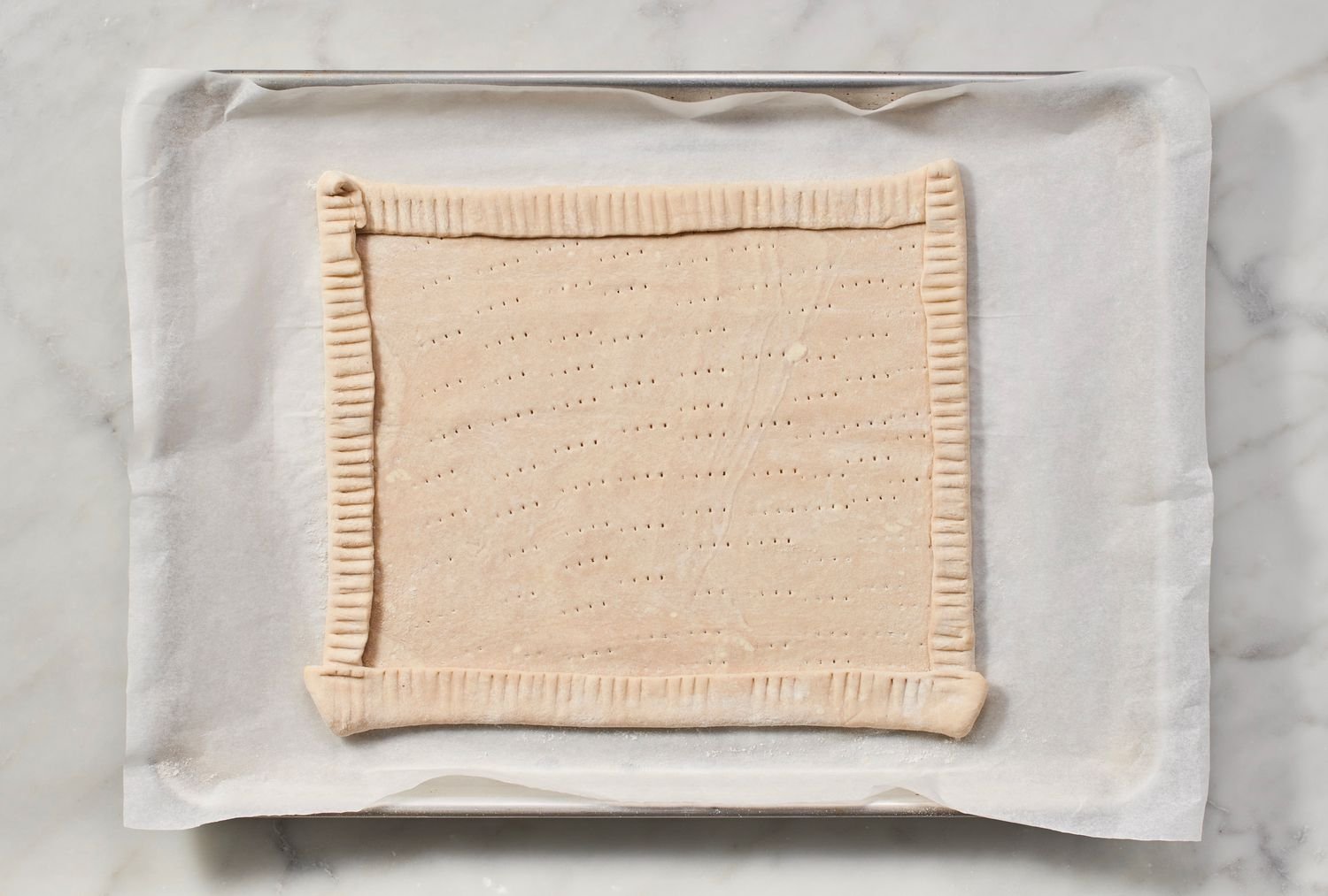A rectangular piece of puff pastry on a parchment paper-lined baking sheet, with fork prick marks and a folded crust edge all around