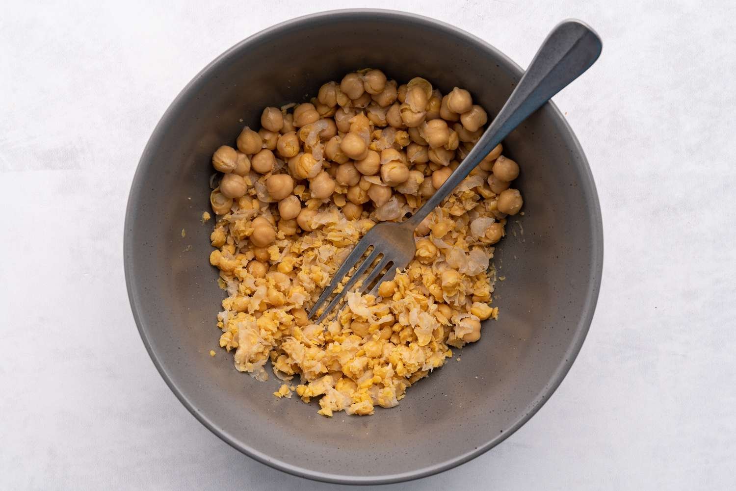 Chickpeas being mashed with a fork in a bowl