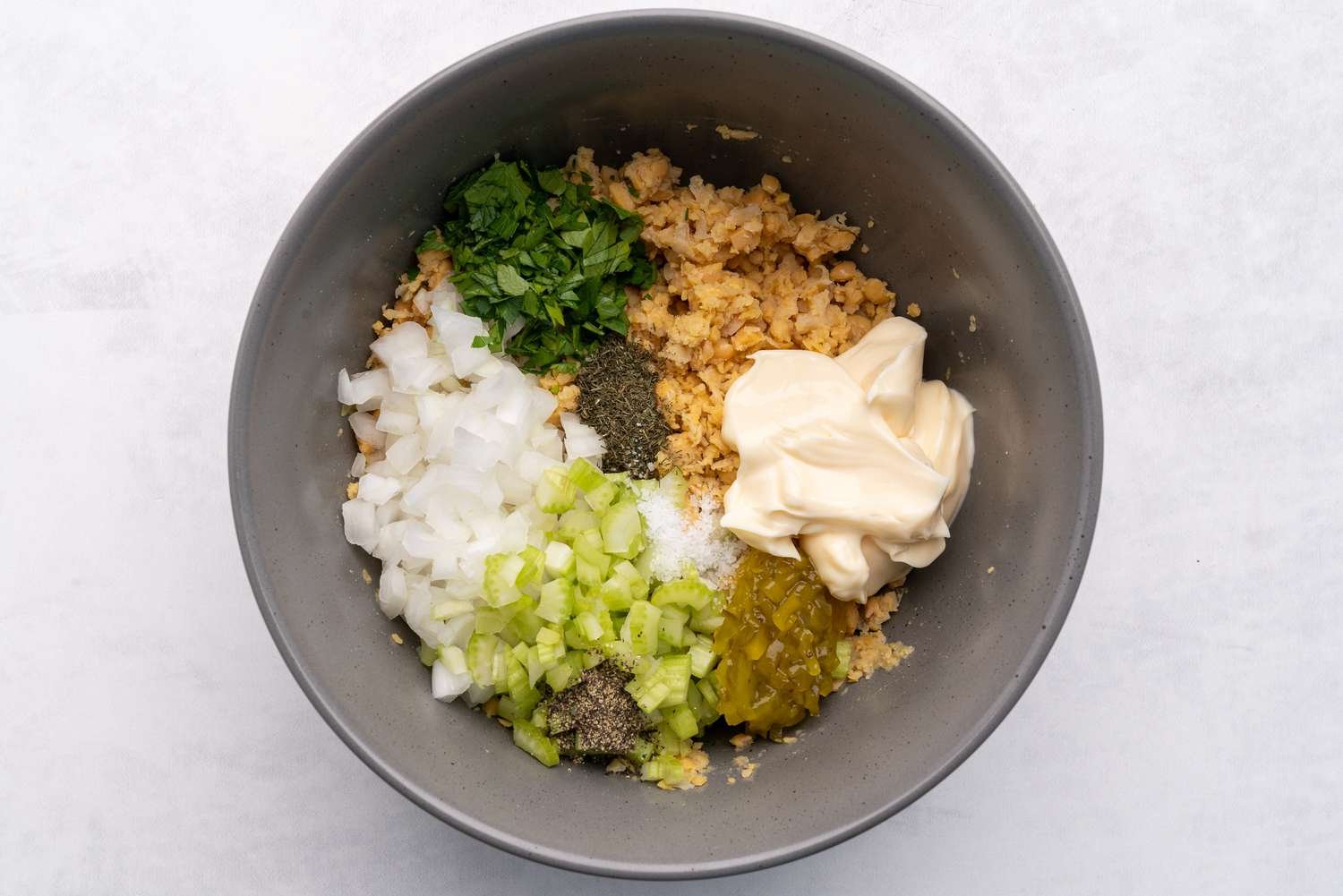 Vegetables, mayonnaise, and seasonings added to mashed chickpeas in the bowl