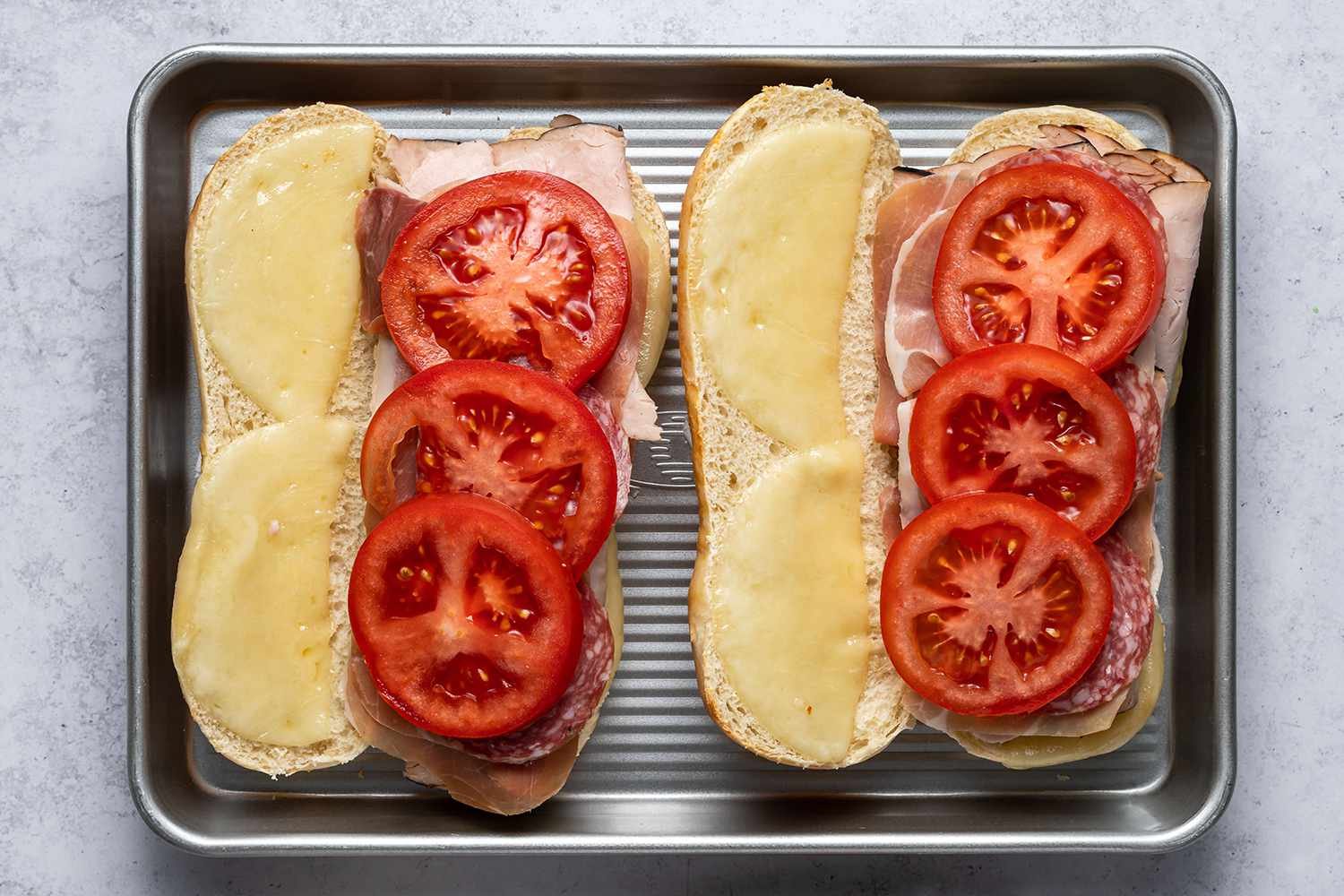 Two slices rolls topped with meats and sliced tomatoes