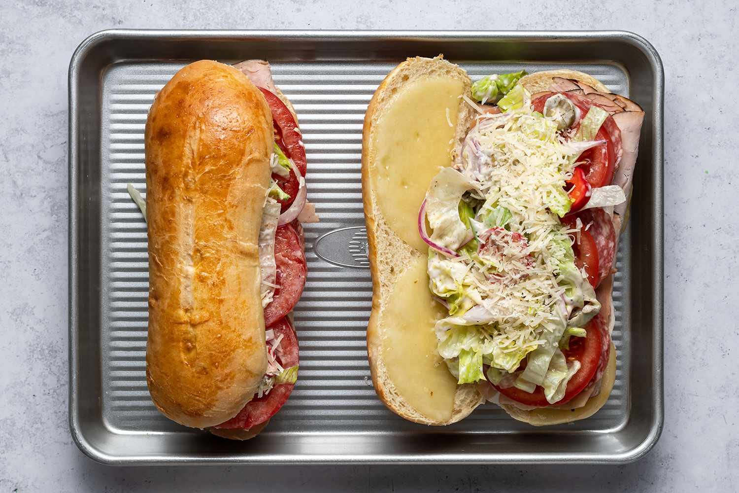 Two finished grinder sandwiches topped with salad and parmesan cheese